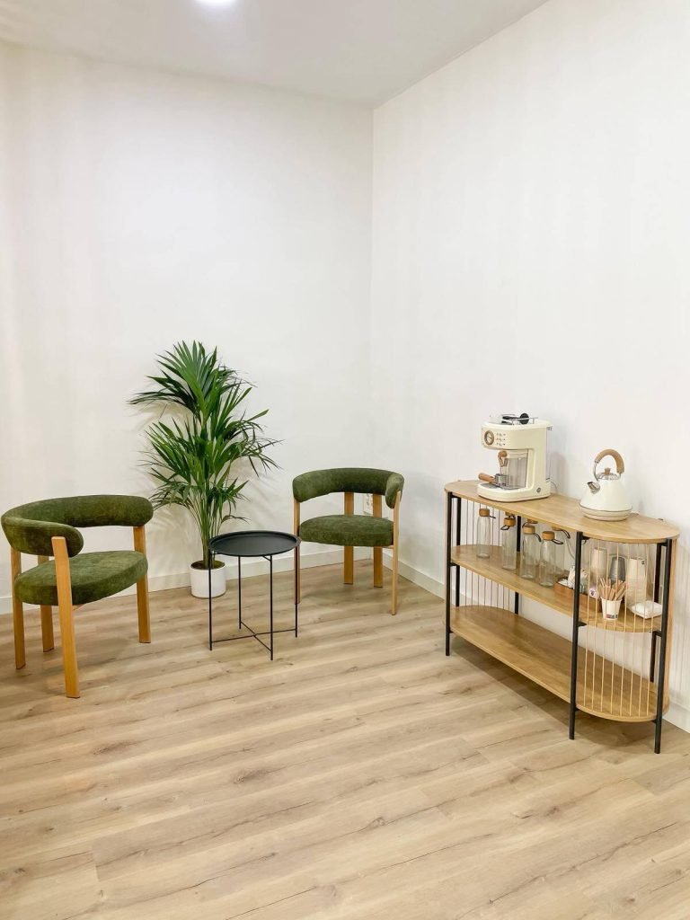 Sala de espera de NG Aesthetics Granada con sillones verdes y rincón de café